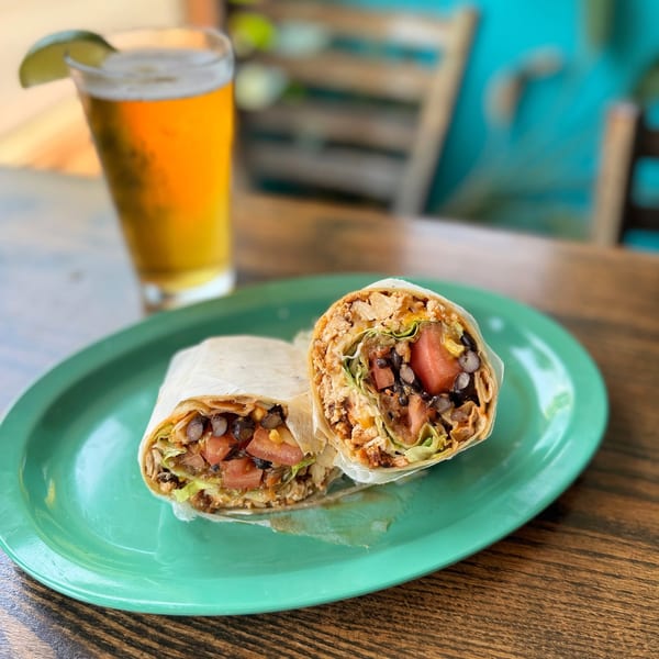 Burrito halves with lettuce, tomatoes, and black beans on a green plate, with a beer.