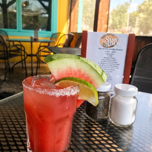 Watermelon margarita with a salted rim and lime on an outdoor patio table.
