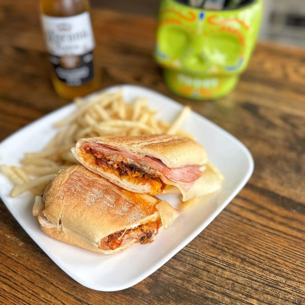 Pressed sandwich with ham, cheese, and pulled pork, served with fries and a beer.