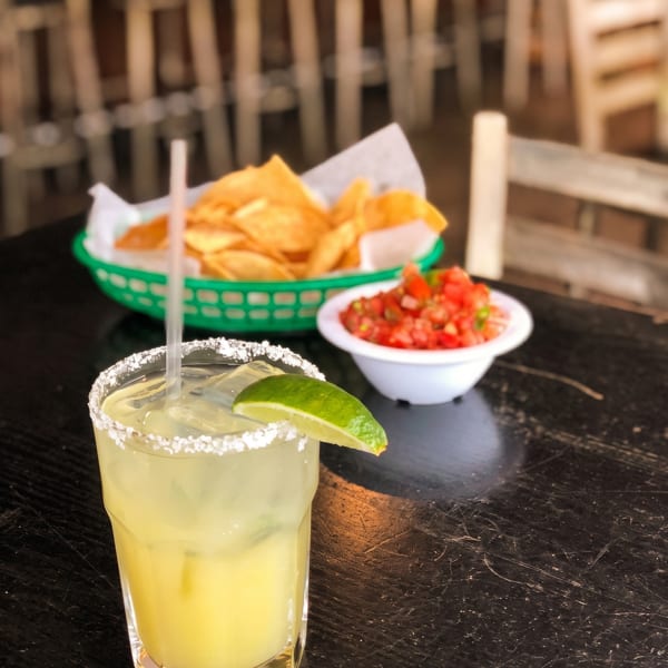 Salt-rimmed margarita with lime, tortilla chips, and salsa on a dark restaurant table.
