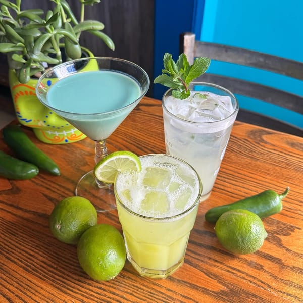 Assortment of three vibrant cocktails with limes and jalapeños on a rustic wooden table.