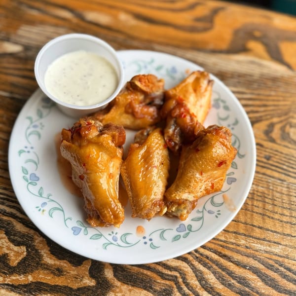Glazed chicken wings on a floral plate with a side of creamy dipping sauce on a wooden table.